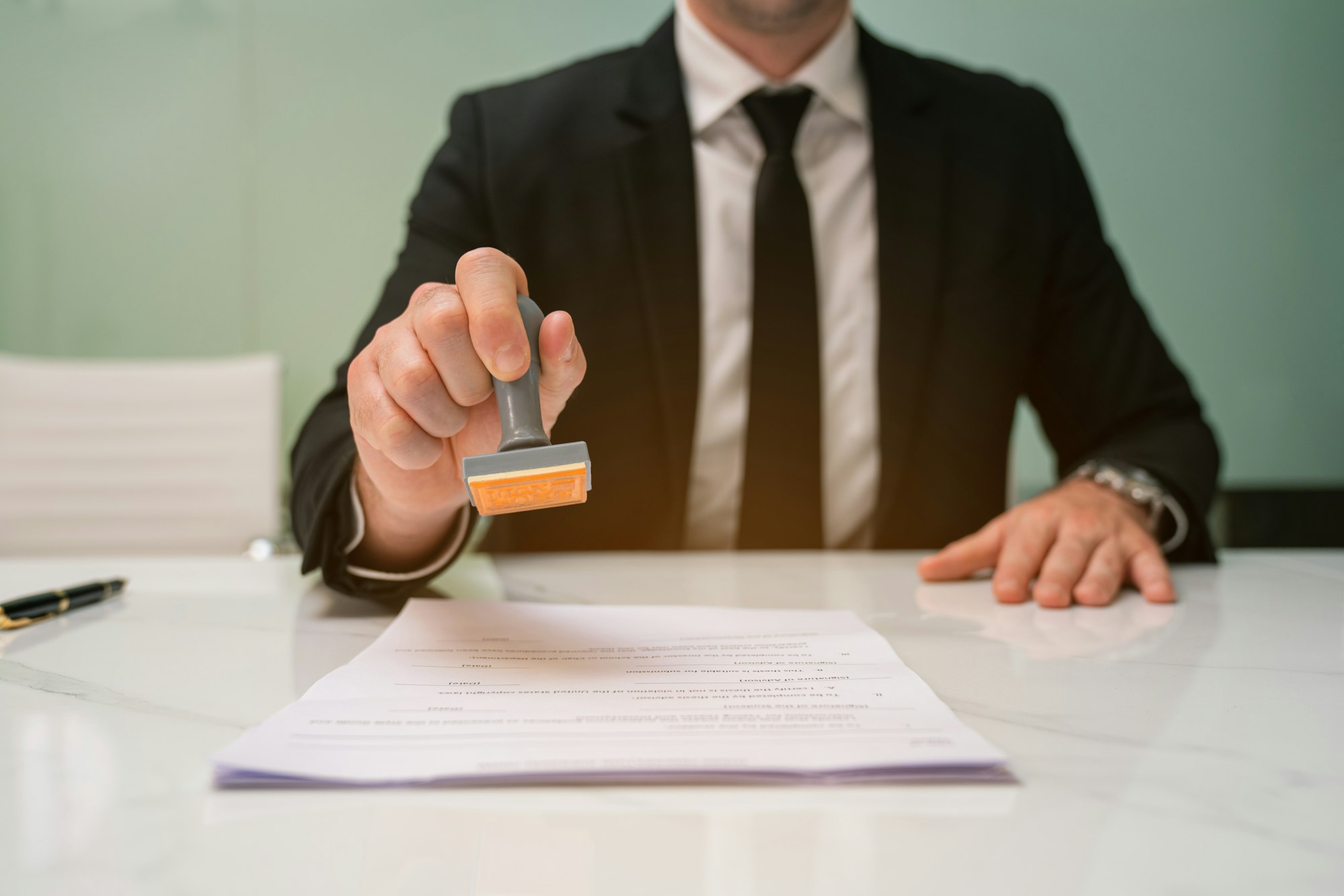 Close-up of a person's hand stamping with approved stamp on certificate document at desk.